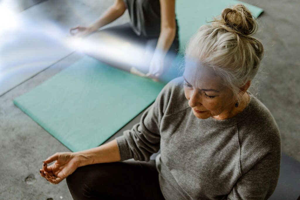 Senior woman meditating beside a yoga mat