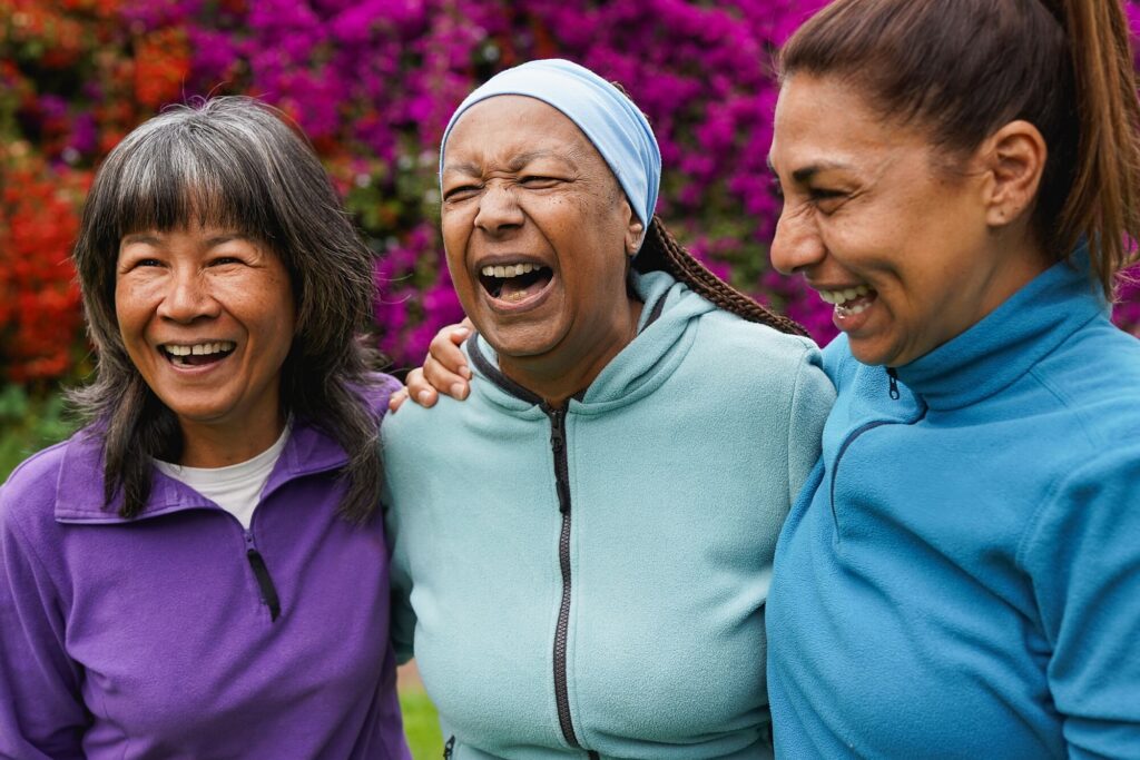 Three women laughing together outdoors in front of flowers